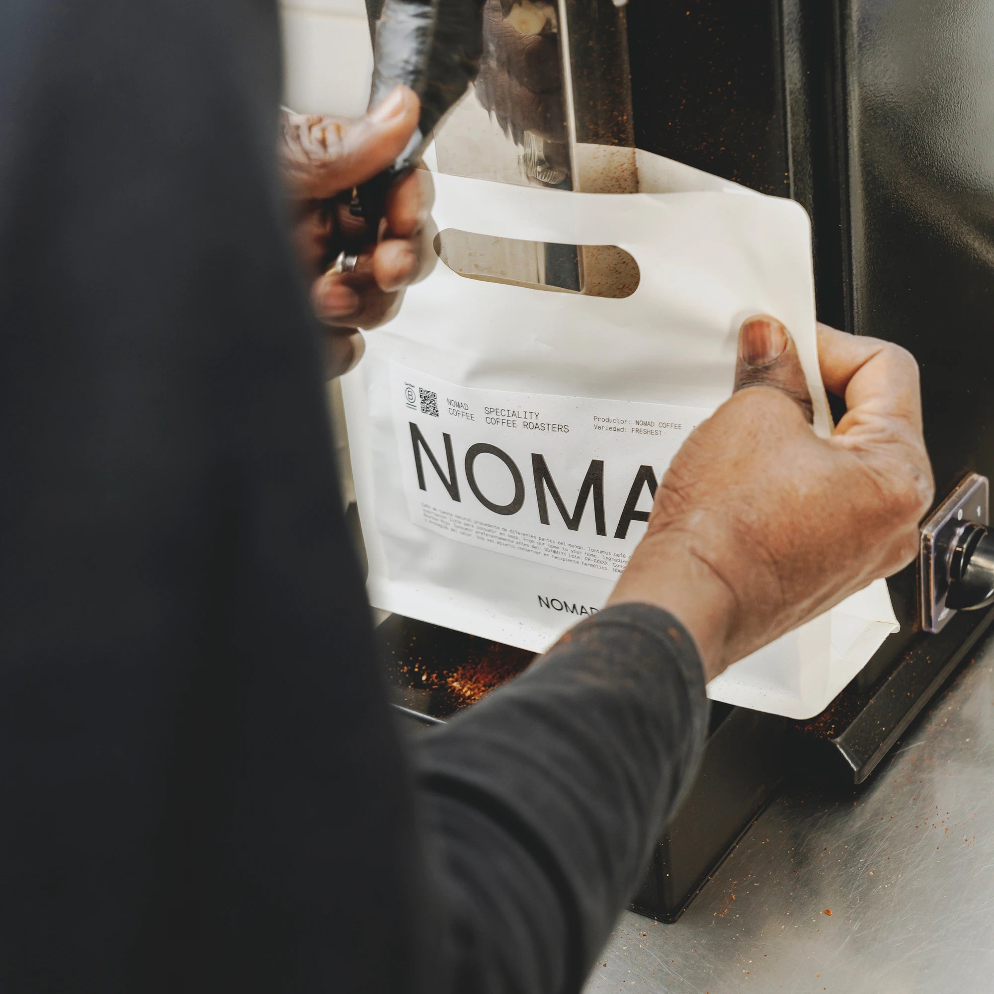 Persona llenando una bolsa blanca de café de Nomad directamente desde la tolva de una máquina dispensadora.