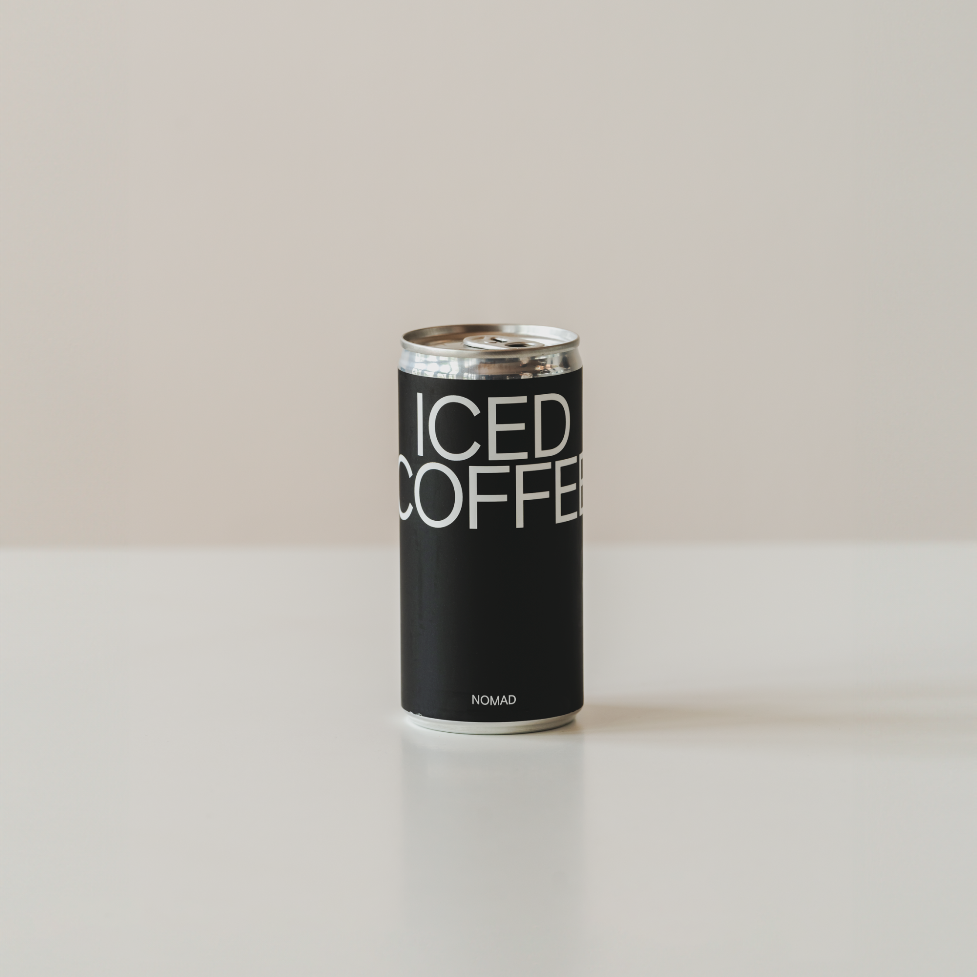 Lata negra de Iced Coffee de Nomad con diseño minimalista y letras blancas, sobre superficie blanca y fondo neutro.